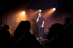 Comedian performing a stand-up comedy routine on stage in a small club with focused audience attention 