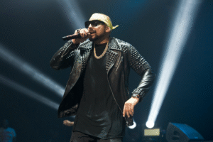 Sean Paul performing live on stage wearing a studded leather jacket and yellow bandana